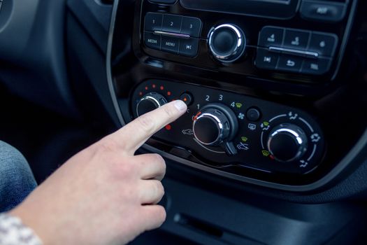 male hand pressing button in modern car. Man adjusts the temperature of the car air conditioner