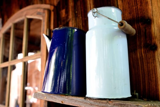Old white milk bubble standing on a wooden shelf and blue jug