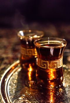 Two cups of steaming hot amber arabic tea on a golden ornate tray.