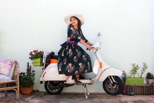 Vintage girl with beautiful floral dress next to a classic motorcycle.