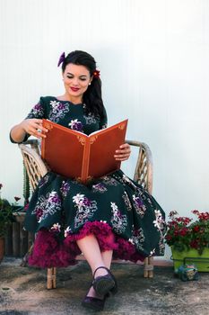 Vintage girl with beautiful floral dress reading a book on a wicker chair.