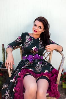 Vintage girl with floral dress posing on a wooden chair.