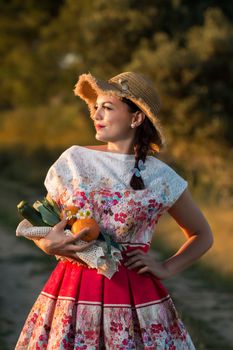 Vintage girl on the countryside with wicker hat gathering groceries.