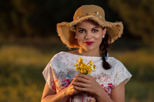 Vintage girl on the countryside with wicker hat with bouquet of flowers.