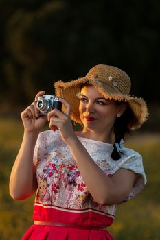 Vintage girl on the countryside with wicker hat with retro camera.