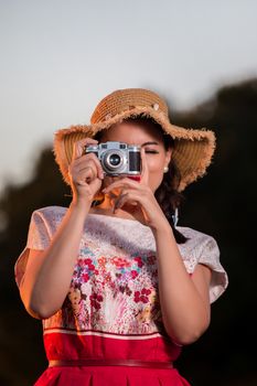 Vintage girl on the countryside with wicker hat with retro camera.