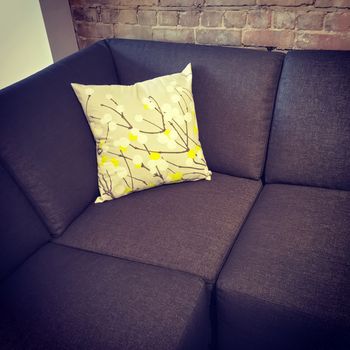 Corner sofa with decorative cushion near brick wall. Modern design.