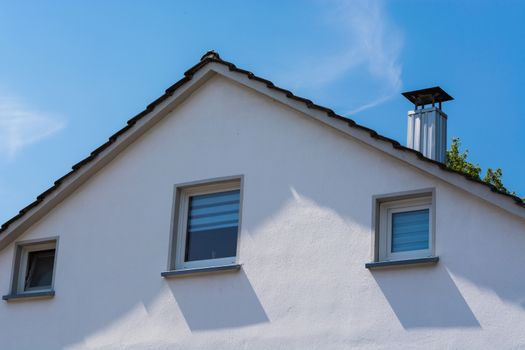 Gable side of a multi-family house of the 60s after modernization, against blue sky.