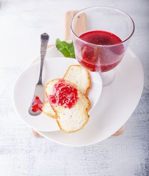 Raspberry jam in bowl with toast on a white surface