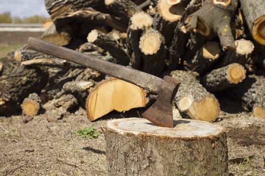 Close up shot of an axe in a stump with firewood in the background.