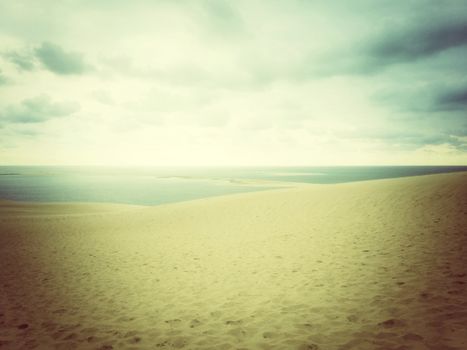 Hazy landscape with sea, sand dunes and cloudy sky.