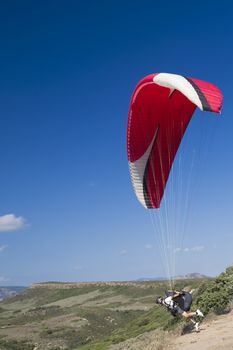 Colorful hang glider in sky over green mountain in Sardinia