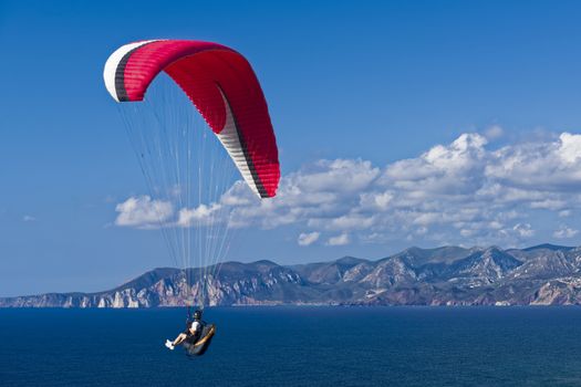 Colorful hang glider in sky over blue sea. Sardinia South West