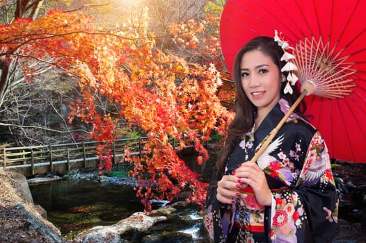 Asian woman wearing traditional japanese kimono with red umbrella in autumn.