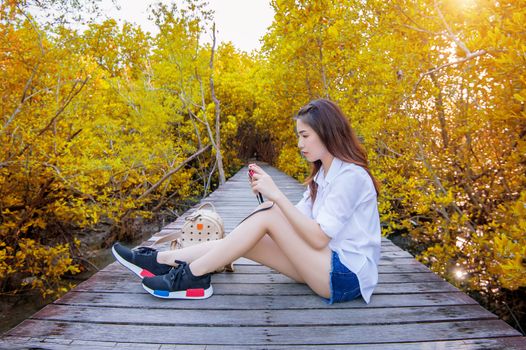 Girl sitting alone and hand holding camera on a the wooden bridge in autumn.