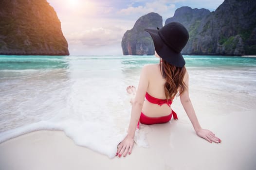 Young woman in red bikini sitting on the beach.