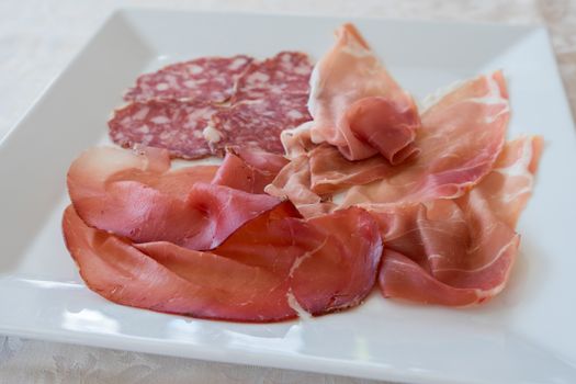 Mix of various Italian salami on white plate servided at restaurant,close up.