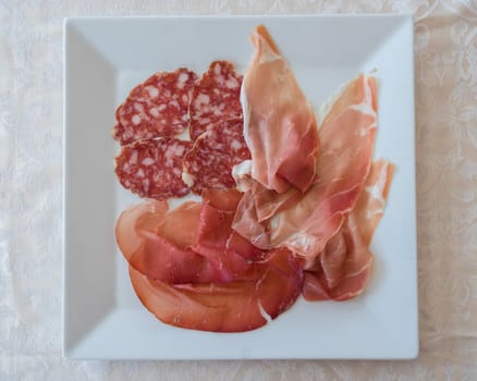 Mix of various Italian salami on white plate servided at restaurant,view from above.