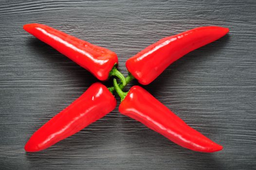 X shaped figure made of four ripe sweet red Kapia peppers on dark shale stone background