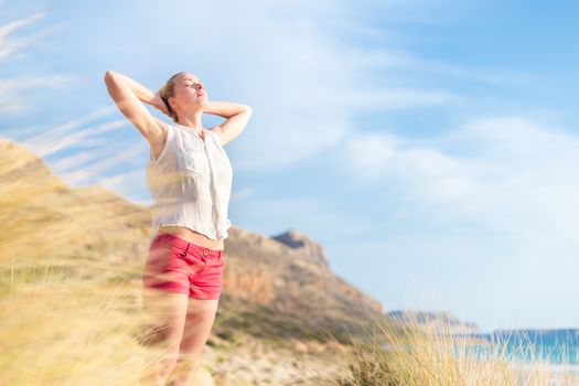 Relaxed woman, arms rised, enjoying sun, freedom and life an a beautiful beach. Young lady feeling free, relaxed and happy. Concept of vacations, freedom, happiness, enjoyment and well being.
