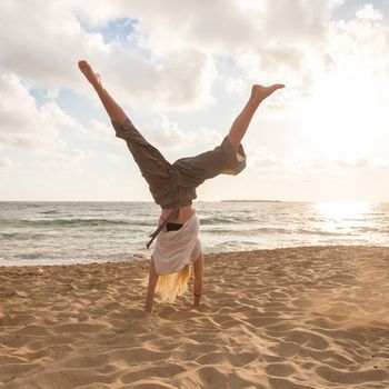 Relaxed woman enjoying sun, freedom and life turning cartwheel on beautiful beach in sunset. Young lady feeling free, relaxed and happy. Vacations, freedom, happiness, enjoyment and well being.