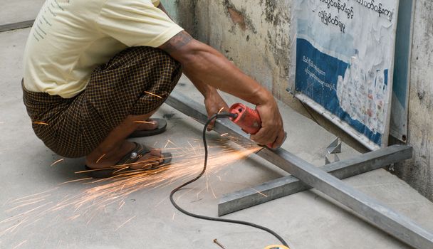 COLOR PHOTO OF WORKER CUTTING STEEL WITH ELECTRIC WHEEL GRINDER