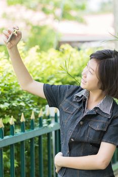 Asian girl with short hair using mobile phone to take selfie outdoor in garden