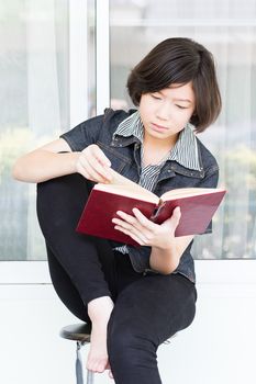Asian girl with short hair reading a book sitting on a chair
