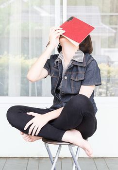 Asian girl with short hair reading a book sitting on a chair