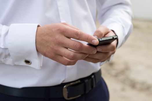 Man in shirt with cufflinks texting on mobile phone at outdoor. Shallow depth of field.