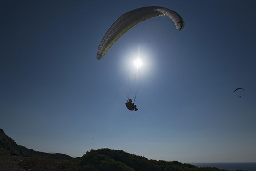 Sport paragliding in backlight with blue sky background and sun in front. Silohuette.
