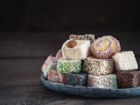 Closeup view of assortment turkish delight in blue trandy plate on dark wooden background. Copy space. Low key