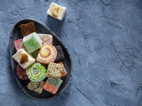 Turkish delight on blue concrete background. Assortment of traditional easten sweet dessert in trandy blue plate. Selective focus. Top view or flat lay. Copy space.