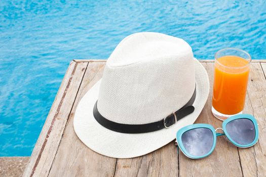Summertime orange juice hat and sunglasses relax near swimming pool.