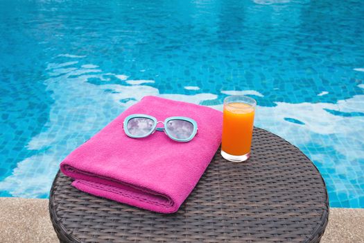 Summertime orange juice hat and sunglasses relax near swimming pool.