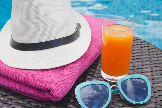 Summertime orange juice hat and sunglasses relax near swimming pool.