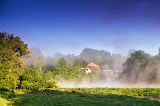 Misty morning on the river. Foggy River landscape through misty marshland on an early morning in spring. House and village in a fog