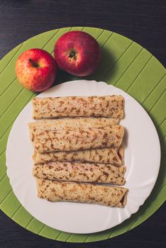 Roasted rolled pancakes on a white round plate and two apples near. Top view . Flat lay.