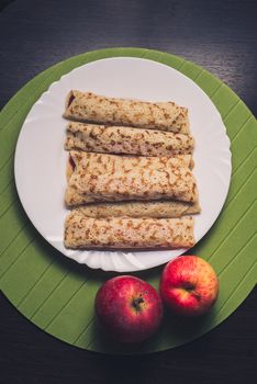 Roasted rolled pancakes on a white round plate and two apples near. Top view . Flat lay.