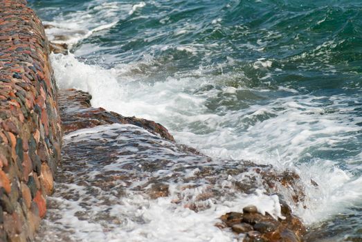 Photo of beautiful clear turquoise sea ocean water surface with ripples and bright splash on stone seascape background, horizontal picture.