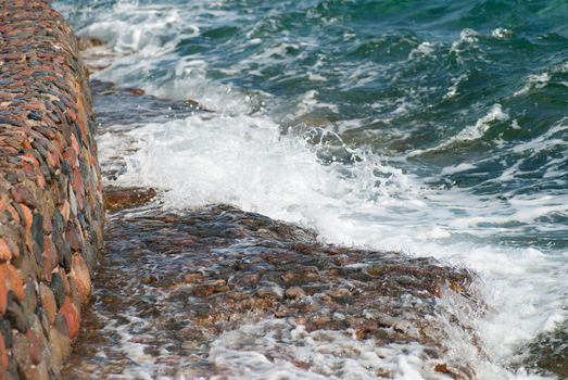 Photo of beautiful clear turquoise sea ocean water surface with ripples and bright splash on stone seascape background, horizontal picture.