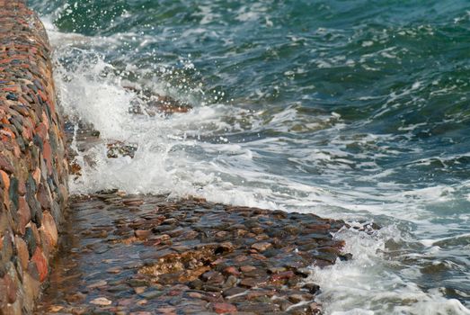 Photo of beautiful clear turquoise sea ocean water surface with ripples and bright splash on stone seascape background, horizontal picture.