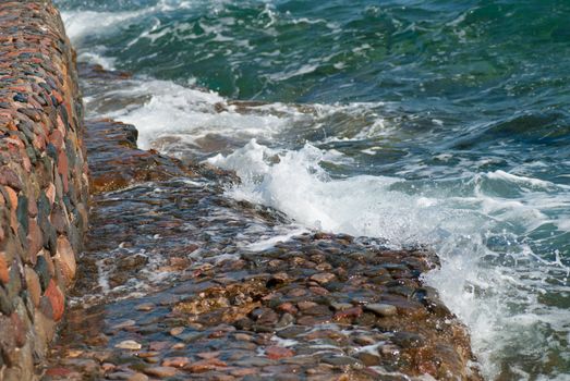 Photo of beautiful clear turquoise sea ocean water surface with ripples and bright splash on stone seascape background, horizontal picture.