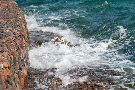 Photo of beautiful clear turquoise sea ocean water surface with ripples and bright splash on stone seascape background, horizontal picture.