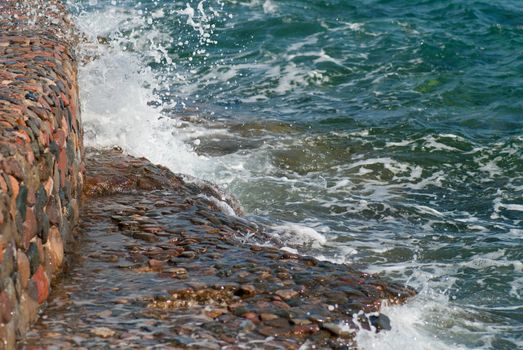 Photo of beautiful clear turquoise sea ocean water surface with ripples and bright splash on stone seascape background, horizontal picture.