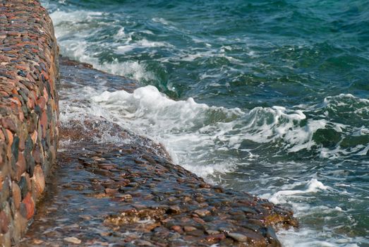 Photo of beautiful clear turquoise sea ocean water surface with ripples and bright splash on stone seascape background, horizontal picture.