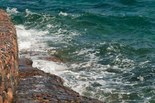 Photo of beautiful clear turquoise sea ocean water surface with ripples and bright splash on stone seascape background, horizontal picture.