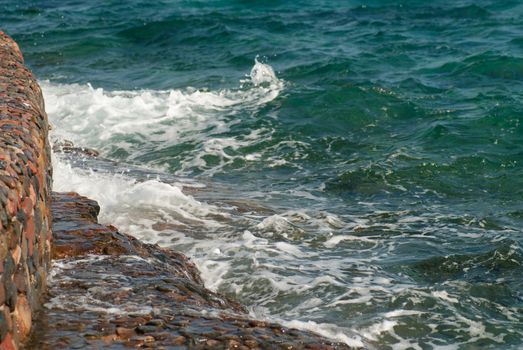 Photo of beautiful clear turquoise sea ocean water surface with ripples and bright splash on stone seascape background, horizontal picture.