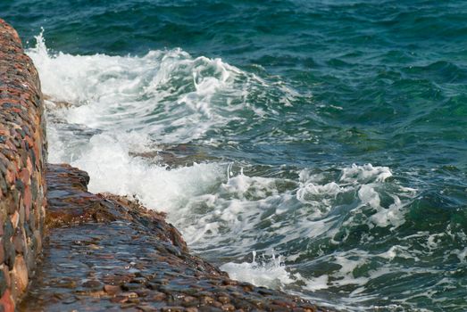 Photo of beautiful clear turquoise sea ocean water surface with ripples and bright splash on stone seascape background, horizontal picture.