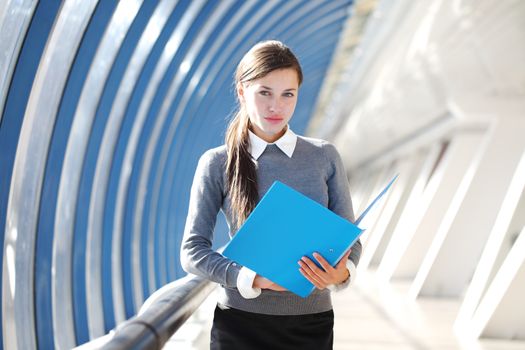 Young Businesswoman with folder standing in corridor of modern office building